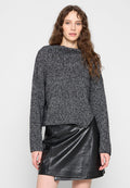 Strickpullover in Schwarz und Grau mit weitem Ausschnitt und langen Ärmeln, kombiniert mit einem schwarzen Leder-Minirock mit asymmetrischem Saum.