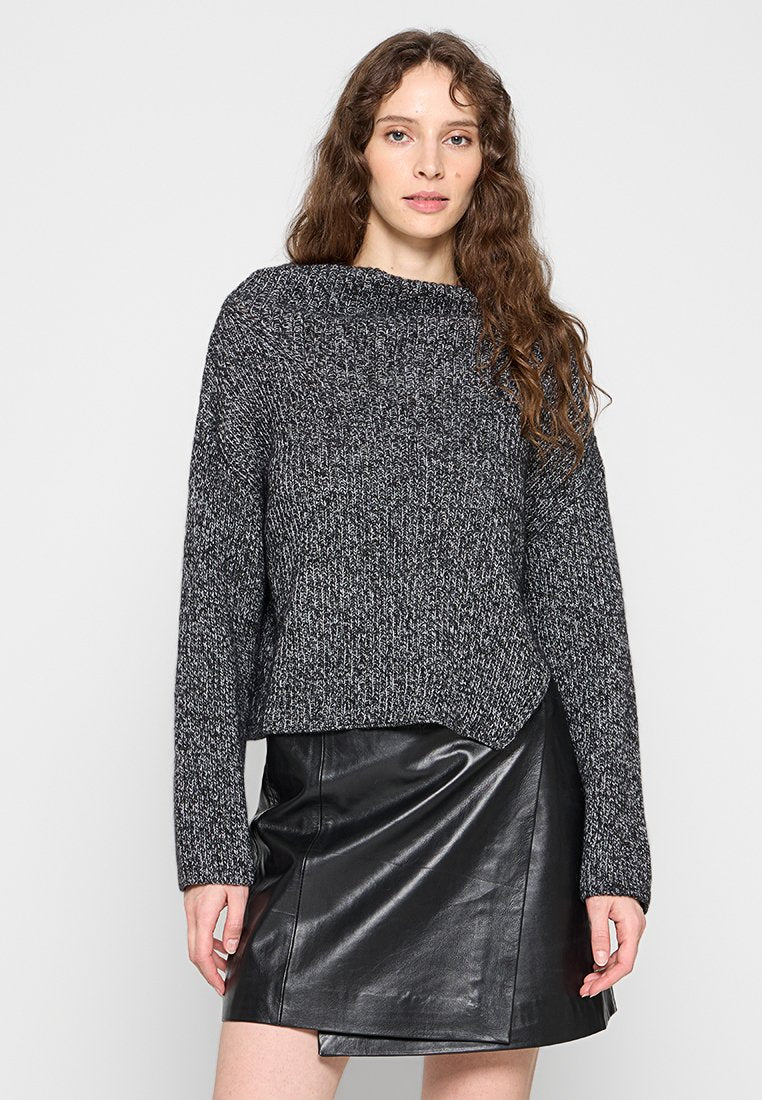 Strickpullover in Schwarz und Grau mit weitem Ausschnitt und langen Ärmeln, kombiniert mit einem schwarzen Leder-Minirock mit asymmetrischem Saum.