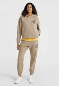 Beige Kapuzenpullover und passende Jogginghose aus weichem Stoff. Der Kapuzenpullover hat eine Fronttasche und ein gedrucktes Logo; die Jogginghose hat elastische Bündchen und Taschen.