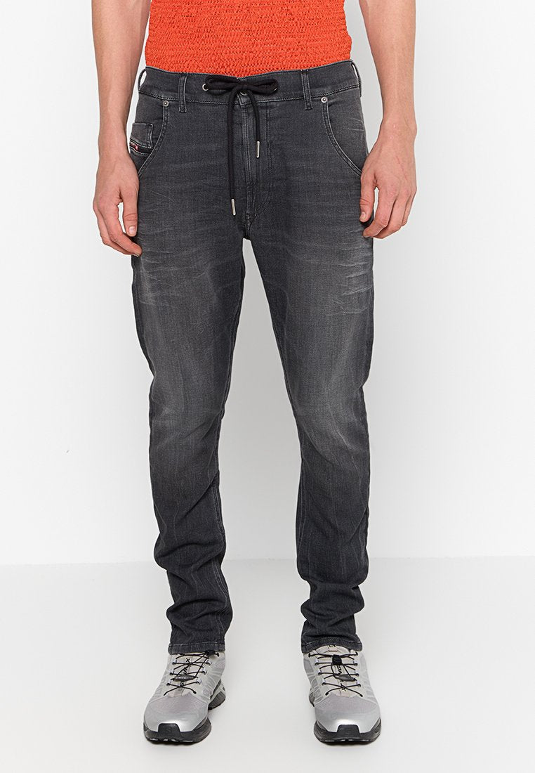 Dunkelgraue Jeans mit schmaler Passform, mit einem Kordelzugbund, vorderen Taschen und subtilen used-Effekten. Dazu graue Schuhe.