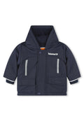 Marineblaue Kinderjacke mit Kapuze, aus synthetischem Material hergestellt. Verfügt über zwei Fronttaschen, reflektierende Einsätze und graue Akzentstreifen.