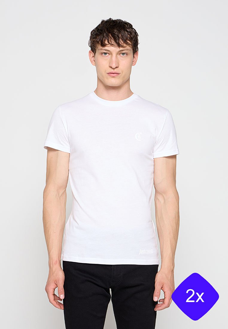 Junger Mann, der ein schlichtes weißes kurzärmeliges T-Shirt und schwarze Hose trägt, steht vor einem weißen Hintergrund.