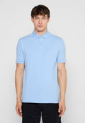 Mann, der frontal steht, trägt ein hellblaues kurzärmliges Poloshirt und schwarze Hose vor einem einfarbigen Hintergrund.