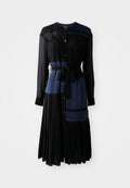 Schwarzes und navy-blaues Kleid mit durchgehender Knopfleiste, langen Ärmeln, Gürtel in der Taille, geschichteten Paneelen und einem plissierten Rock. Mit Spitzenakzenten.