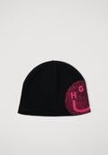 Schwarze Strickmütze mit pinkem pixeliertem Design und teilweise sichtbarem "HUGO"-Text auf einer Seite sowie kleinem schwarzem "HUGO"-Logo in der Nähe des Randes.