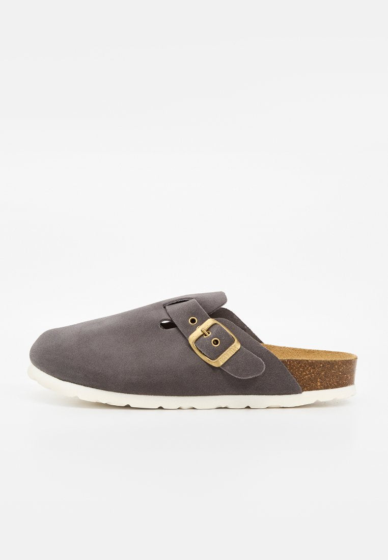 Grauer Veloursleder-Slipper mit verstellbarer Schnalle, Korkfußbett und weißer Gummisohle, von der Seite auf weißem Hintergrund gezeigt.