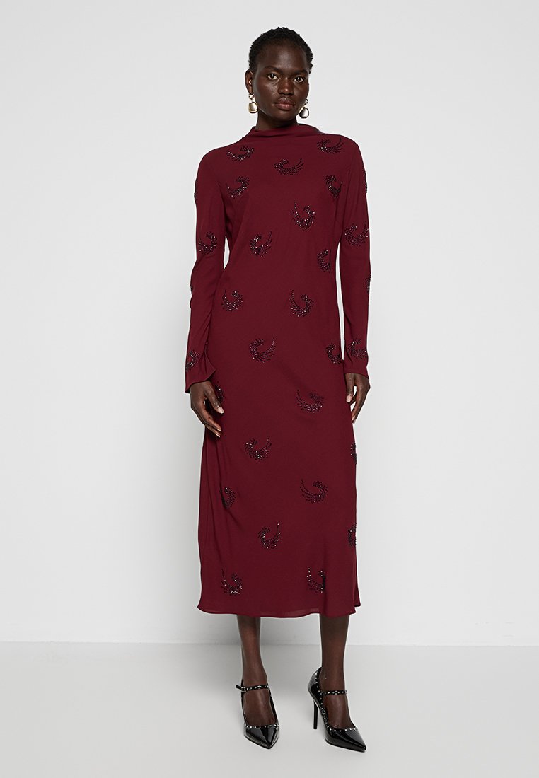 Burgunderrotes Langarmkleid mit geradem Schnitt, das mit perlenbesetzten Wirbelmustern verziert ist. Hergestellt aus glattem Stoff mit einer weichen Textur.