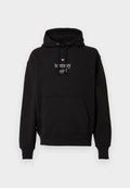 Schwarzer Hoodie mit vorderer Kängurutasche, Kapuze mit Kordelzug, kleinem Sternlogo und weißem Text "tommy girl" auf der Brust.