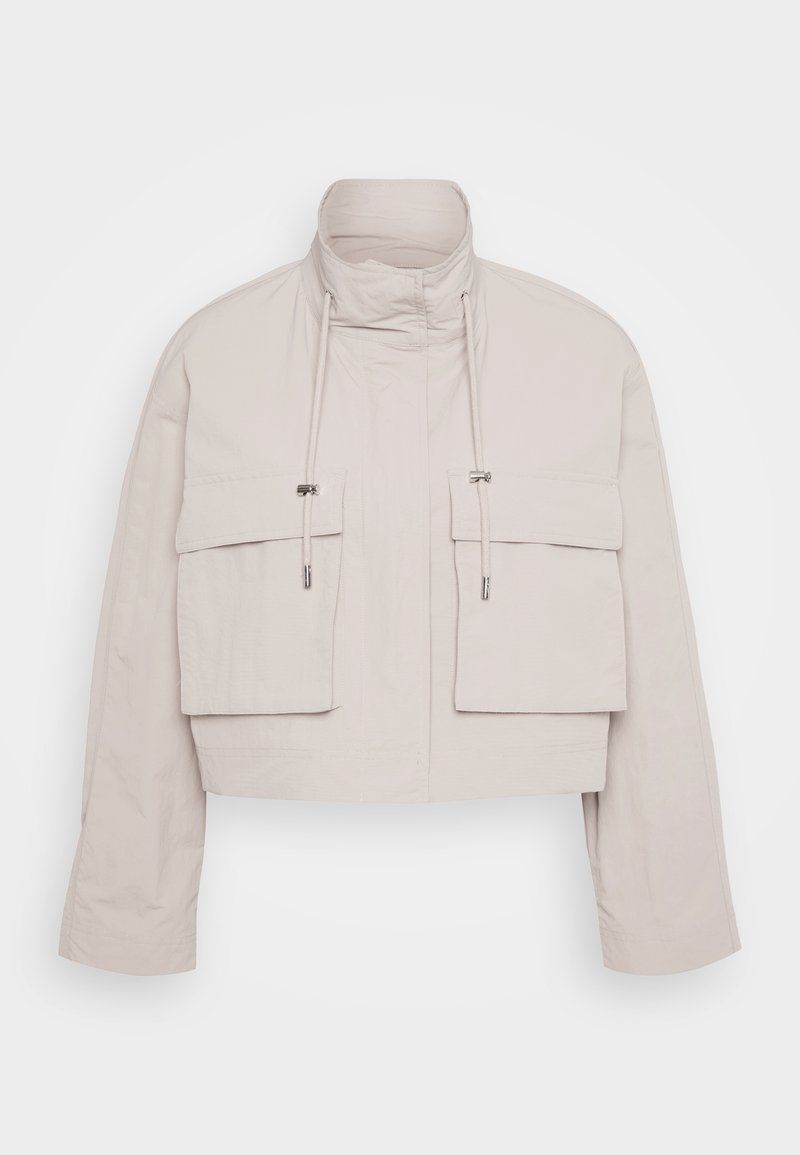 Kurze Jacke aus hellbeigem Stoff mit hohem Kragen, zwei aufgesetzten Fronttaschen und verstellbaren Kordeln für einen sicheren Sitz.