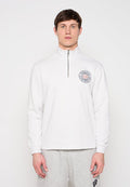 Mann trägt weißen Sweatshirt mit Viertel-Reißverschluss und rundem Logo auf der linken Brust sowie helle graue Jogginghose und steht vor einem einfarbigen Hintergrund.