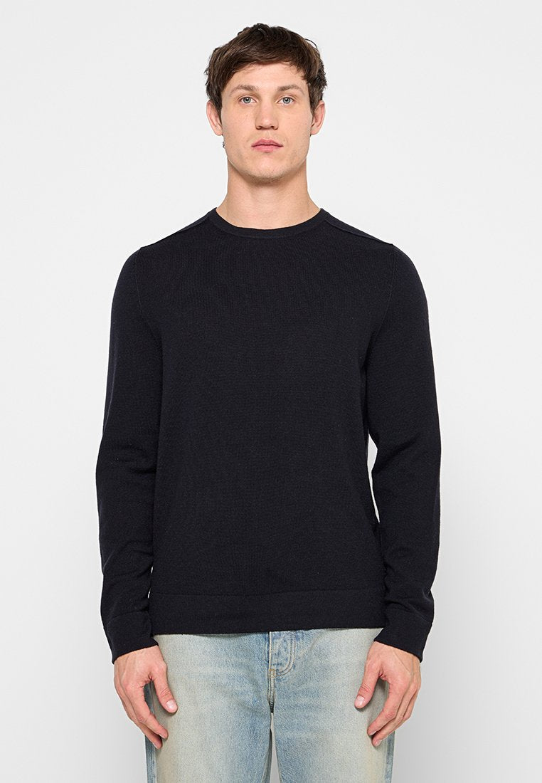 Schwarzer, gerippter Pullover mit langen Ärmeln, Rundhalsausschnitt und lockerem Schnitt, gefertigt aus strukturiertem Strickstoff. Kombiniert mit hellblauen Jeans.
