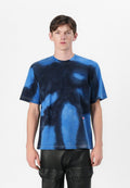 Blaues Batik-T-Shirt mit Rundhalsausschnitt und kurzen Ärmeln, hergestellt aus weichem Stoff mit kontrastierenden dunklen Mustern. Kleines Logo-Detail am Saum.