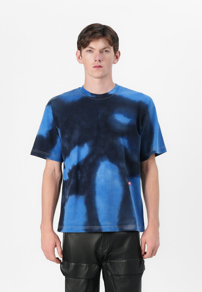 Blaues Batik-T-Shirt mit Rundhalsausschnitt und kurzen Ärmeln, hergestellt aus weichem Stoff mit kontrastierenden dunklen Mustern. Kleines Logo-Detail am Saum.