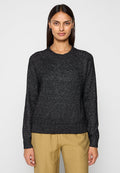 Schwarzer Strickpullover mit Rundhalsausschnitt, langen Ärmeln und strukturierter Oberfläche. Kombiniert mit hellen, locker sitzenden Hosen.