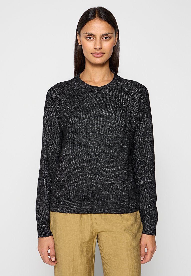 Schwarzer Strickpullover mit Rundhalsausschnitt, langen Ärmeln und strukturierter Oberfläche. Kombiniert mit hellen, locker sitzenden Hosen.