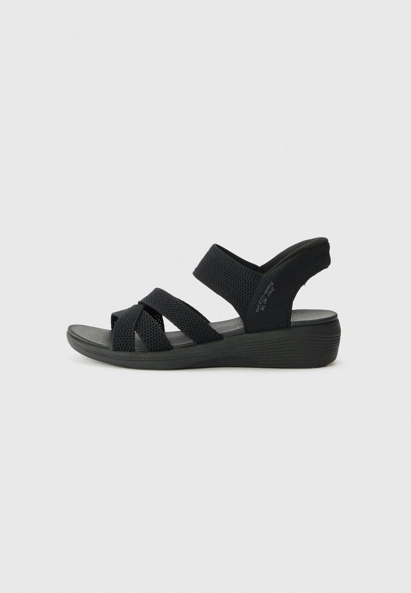 Schwarze Sandalen mit Keilabsatz, ausgestattet mit Überkreuzriemen aus Netzgewebe. Die weiche Innensohle und die Gummisohle erhöhen den Komfort und die Unterstützung.