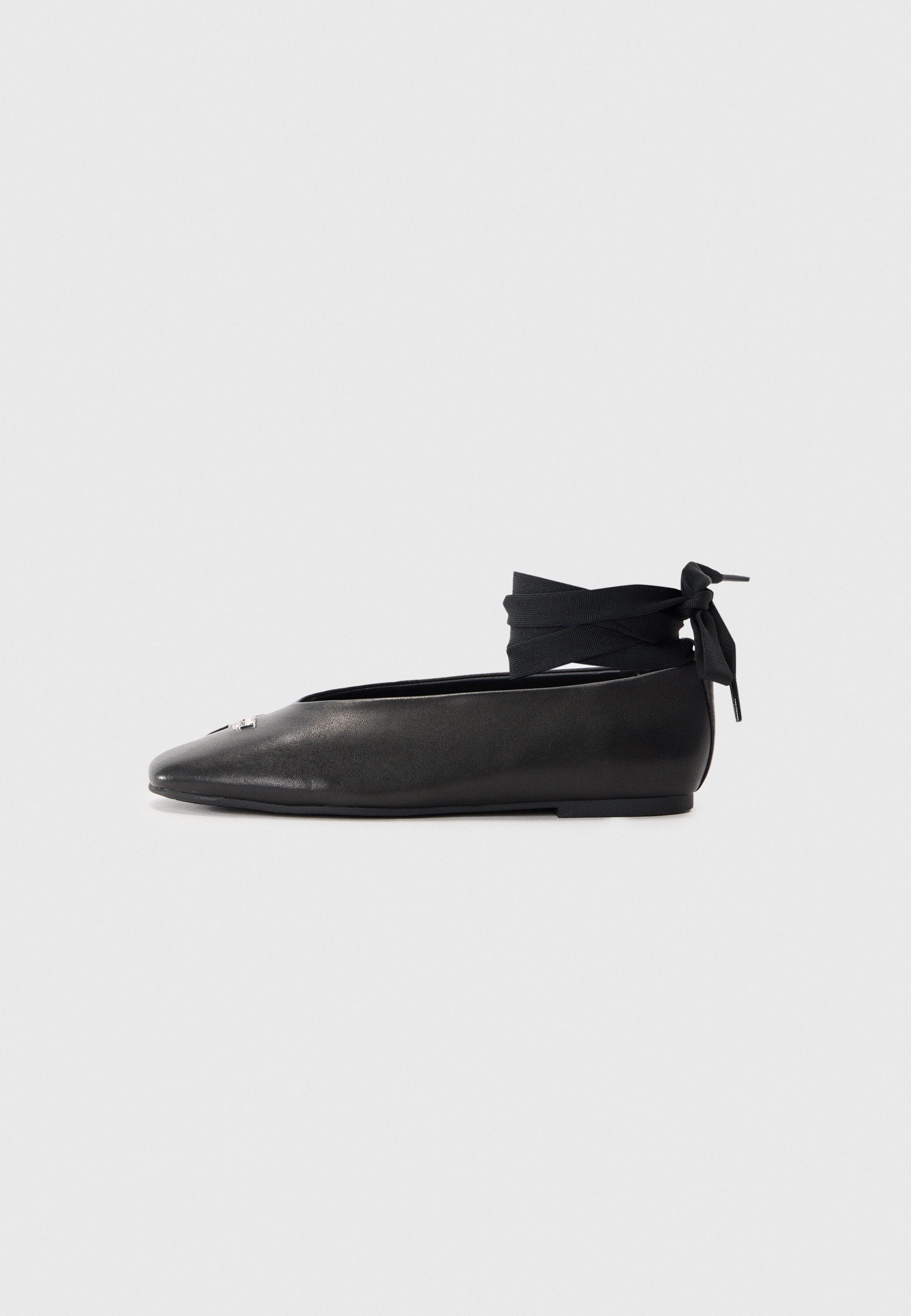 Schwarze Leder-Ballerinas mit spitzem Zehenbereich, ausgestattet mit einem gewebten Stoff-Ankle-Tie und einem kleinen dekorativen Akzent auf der Zehe.