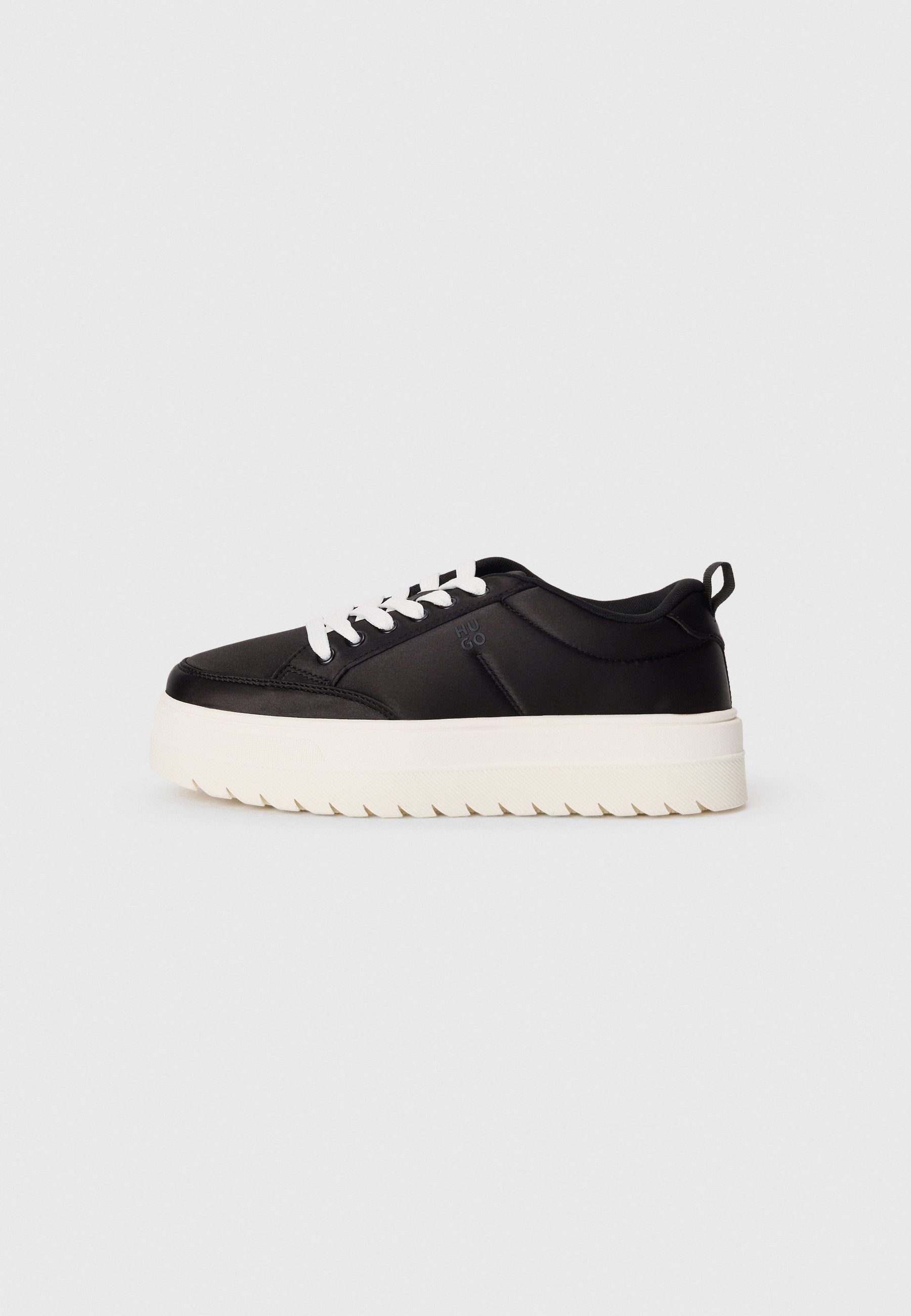 Schwarzer sportlicher Sneaker aus glattem Stoff, mit weißen Schnürsenkeln, einer klobigen weißen Sohle und einer strukturierten Gummisohle.
