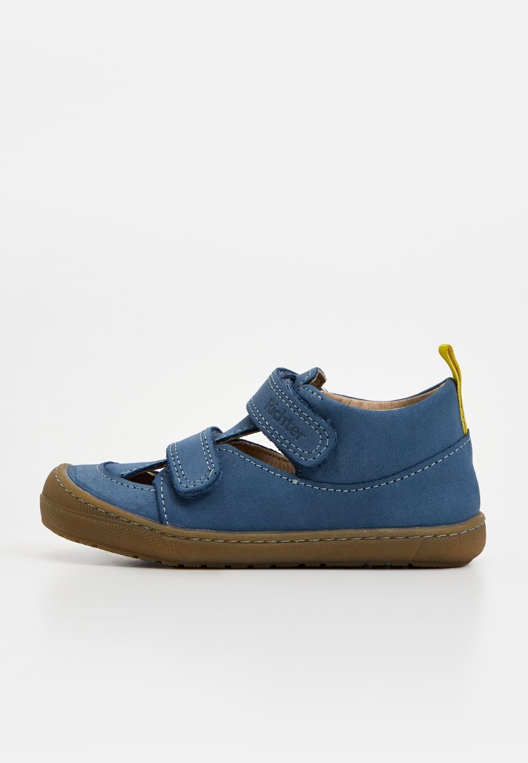 Blauer Kleinkindschuh mit brauner Gummisohle, zwei Klettverschlüssen und gelbem Zuglasche an der Ferse, dargestellt auf weißem Hintergrund.