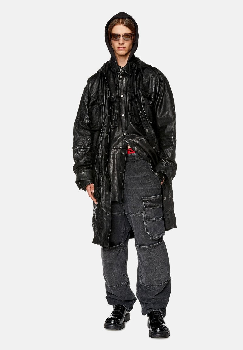 Schwarzer Leder-Mantel in Übergröße mit strukturierter Oberfläche, über einem schwarzen Hemd mit Knöpfen getragen. Dunkelgraue Cargo-Hosen und glänzende schwarze Schuhe runden den Look ab.