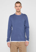 Marineblauer Pullover mit langen Ärmeln, strukturierter Oberfläche und weißem Besatz am Hals, kombiniert mit hellbraunen Hosen.