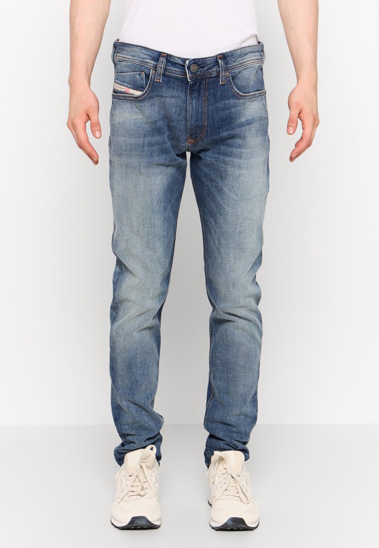 Blaue Jeans aus Denim mit einem ausgewaschenen Look, fünf Taschen und einem Knopfverschluss. Getragen mit beigen Sneakers.