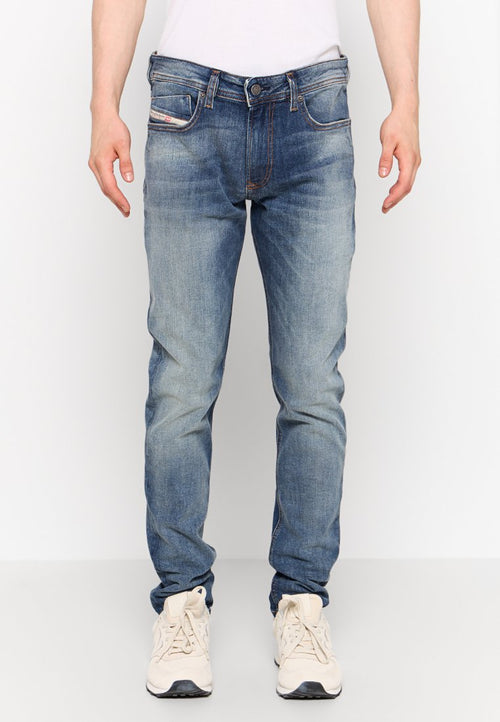 Blaue Jeans aus Denim mit einem ausgewaschenen Look, fünf Taschen und einem Knopfverschluss. Getragen mit beigen Sneakers.