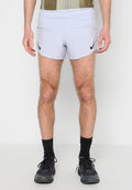 Mann, der hellgraue Nike-Laufshorts, schwarze Sportschuhe und schwarze Socken trägt, steht vor einem schlichten weißen Hintergrund.