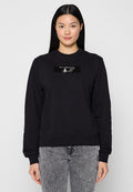 Schwarzes Sweatshirt mit Rundhalsausschnitt und langen Ärmeln, versehen mit einem rechteckigen Pailletten-Patch auf der Vorderseite. Getragen mit grauen Jeans.