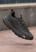 Dunkelgrauer Laufschuh mit strukturierter Oberseite, kontrastierenden roten Schnürsenkeln und robustem Laufsohle. Mit Logo an der Seite und Lasche an der Ferse.