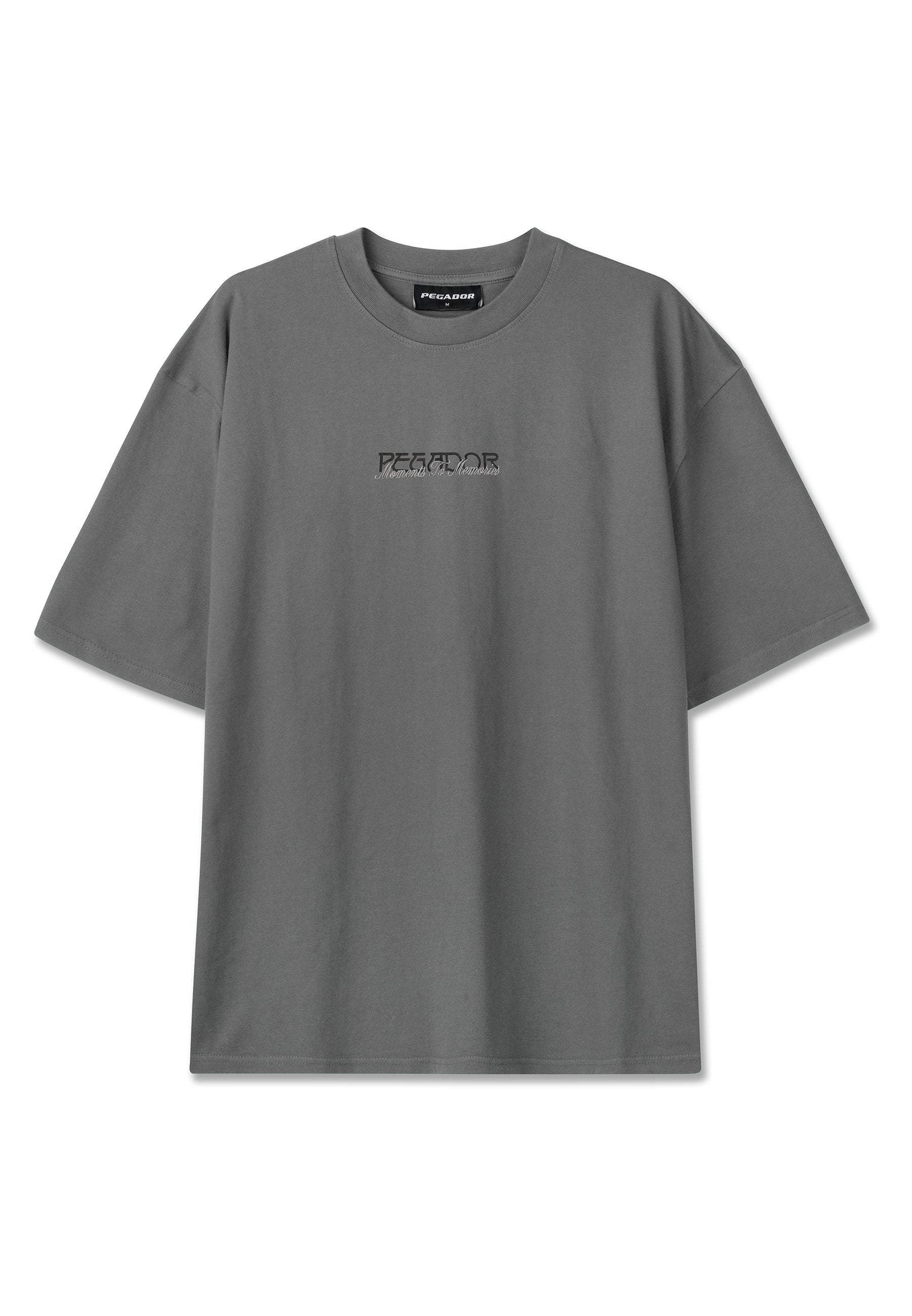 Graues T-Shirt mit kurzen Ärmeln und Rundhalsausschnitt, mit schwarzem und weißem "PEGADOR"-Logo und kleinem Text mittig auf der Brust.