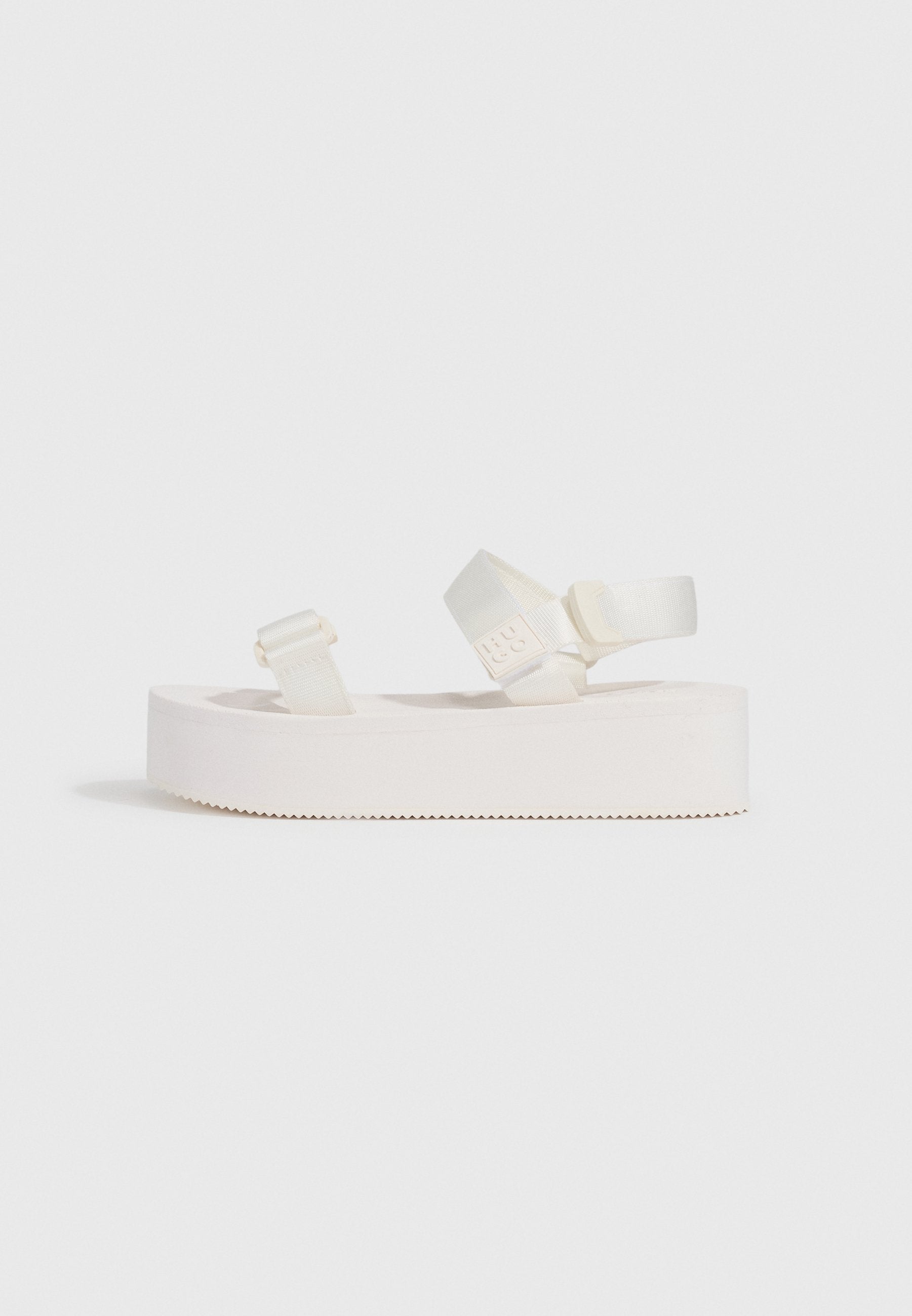 Weiße Plateau-Sandalen mit zwei verstellbaren Riemen. Weiches Material mit einer strukturierten Sohle, die ein Zickzackmuster für besseren Halt aufweist.