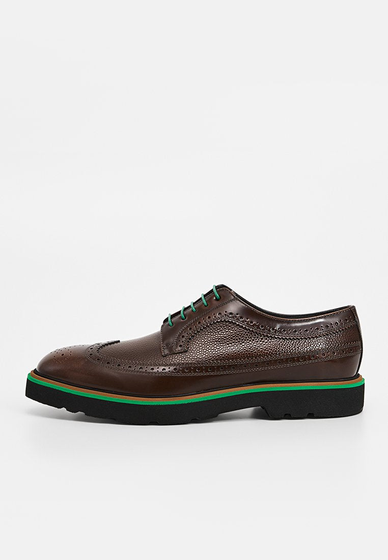 Braune Brogue-Lederschuhe mit dekorativen Perforationen, grünen Schnürsenkeln und einer kontrastierenden grünen und braunen Sohle. Flaches Profil und strukturiertes Design.