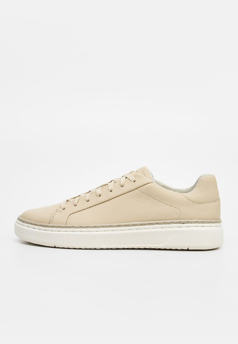 Beiger Low-Top-Ledersneaker mit weißer dicker Sohle und beigen Schnürsenkeln auf schlicht weißem Hintergrund.