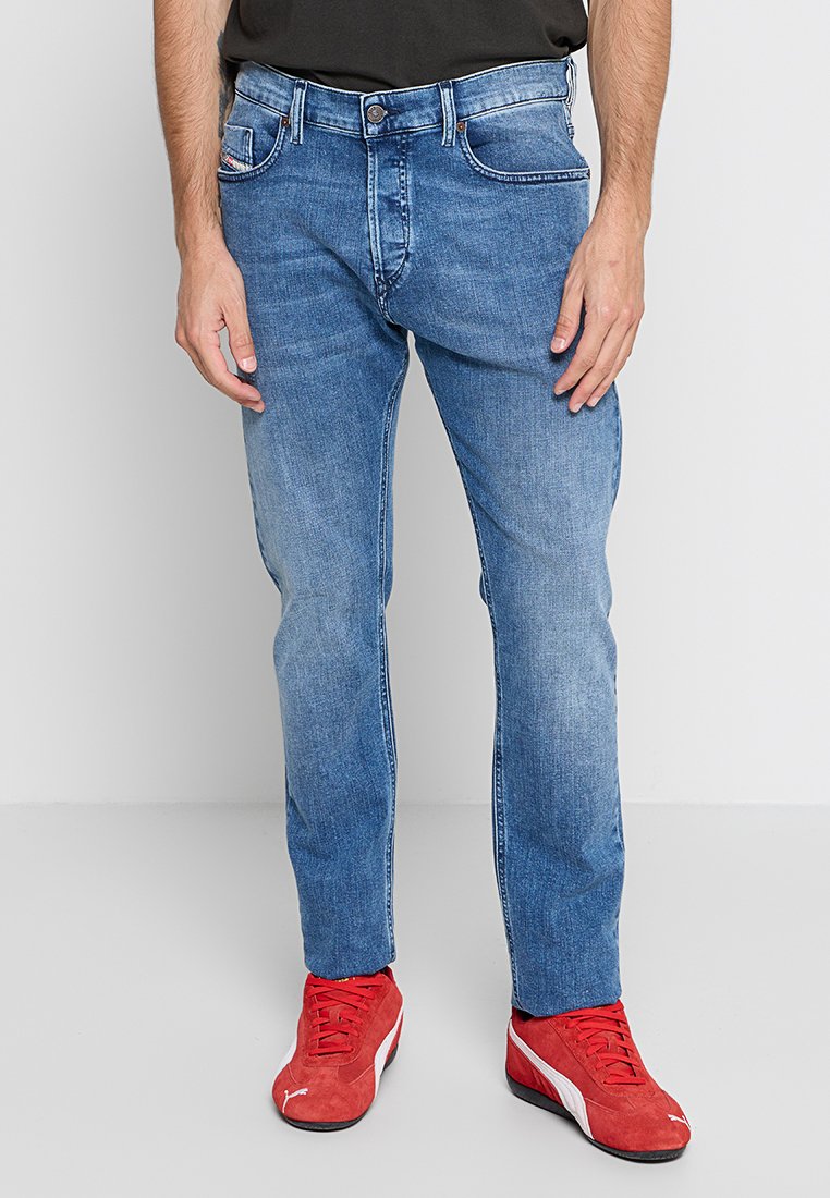 Blaue Denim-Jeans mit geradem Bein, ausgestattet mit einem klassischen Five-Pocket-Design und einem ausgewaschenen Finish, kombiniert mit roten Sportschuhen.