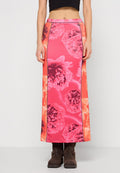 Lange, floral gemusterte Rock in leuchtendem Pink mit glatter Textur, versehen mit schwarzen Seitennaht und Hakenverschluss, kombiniert mit braunen Stiefeletten.