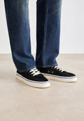 Schwarze Leinenschuhe mit weißen Schnürsenkeln, blauen Akzenten und Gummisohlen, getragen mit dunklen Denim-Jeans im geraden Schnitt und subtiler Ausbleichung.