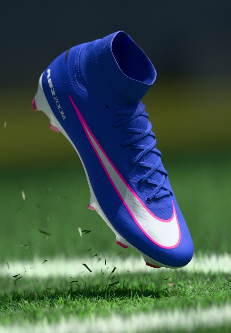 Blauer Fußballschuh mit weißem und pinkem Nike-Swoosh, Schnürsenkel gebunden, und dem Text "AIR ZOOM", der über einem Grasboden mit verstreuten Grashalmen schwebt.