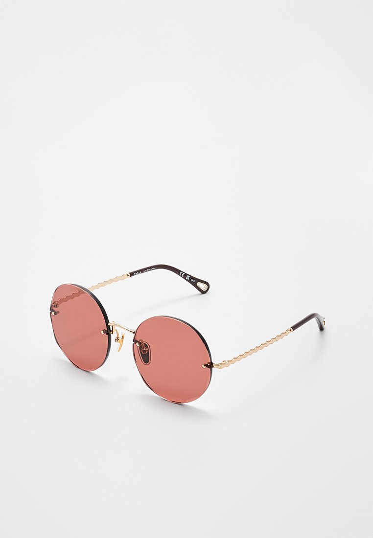Runde Sonnenbrille mit rosa Gläsern, dünnen goldenen Rahmen und schwarzen Bügelenden vor weißem Hintergrund.