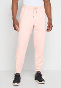 Mann trägt hellrosa Sweatpants mit Kordelzug und schwarze Sportschuhe, steht vor einem schlichten Hintergrund.
