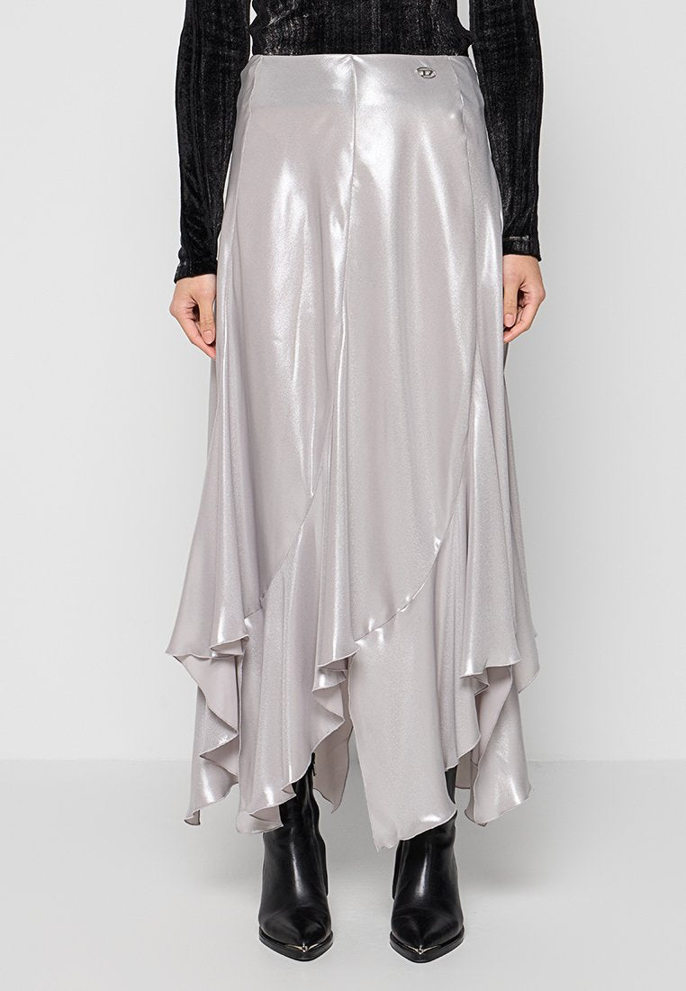 Glänzender silberner asymmetrischer Midirock mit Rüschensaum, getragen mit schwarzem Samtoberteil und schwarzen spitzen Stiefeln auf einfarbigem Hintergrund.