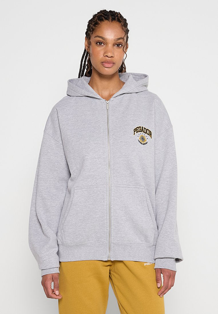 Grauer Reißverschluss-Hoodie mit großer Kapuze, Fronttaschen und gesticktem Logo. Weicher Stoff und lässiger Schnitt, kombiniert mit senfgelben Hosen.