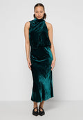 Smaragdgrünes Samtkleid ohne Ärmel mit hohem Ausschnitt, tailliertem Oberteil und fließendem Saum. Schwarze Slippers runden den Look ab.
