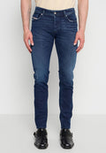 Mann trägt dunkelblaue Slim-Fit-Jeans und schwarze Leder-Monk-Strap-Schuhe vor einfarbigem Hintergrund.