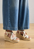 Goldene Riemchen-Wedge-Sandalen mit einem gewebten Jute-Sockel. Sie besitzen breite Kreuzriemen und ein rundes Zehen-Design. Getragen mit hellblauen weit geschnittenen Jeans.