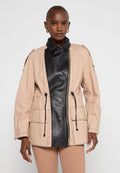Beige Stoffjacke mit einem schwarzen Leder-Vorderteil, ausgestattet mit zwei Fronttaschen, einem verstellbaren Bund und Schulterklappen. Mit Reißverschluss.