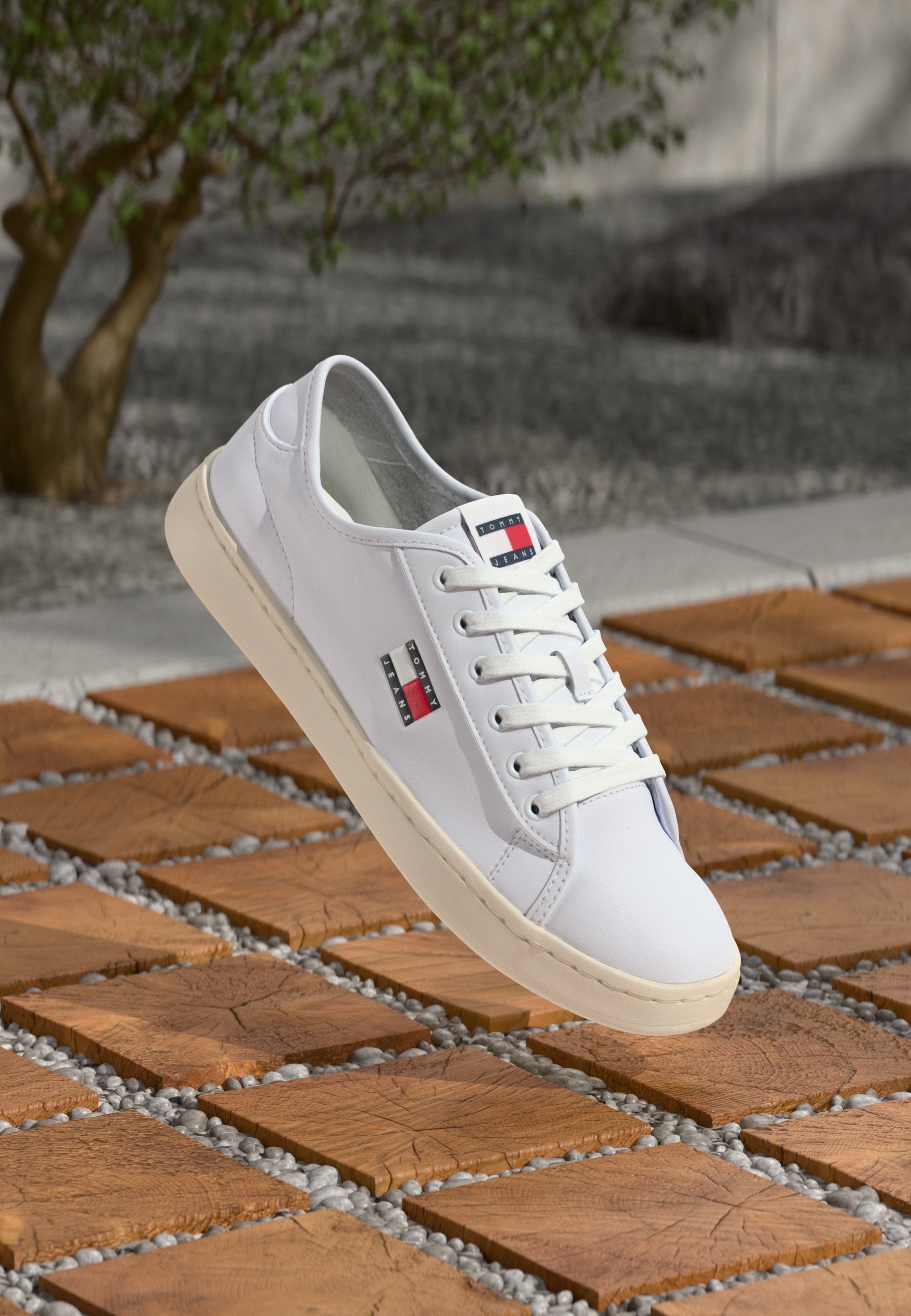 Weiße Leder-Sneaker mit minimalistischem Design, Gummisohle und zwei Markentabs mit roten und blauen Akzenten. Schnürsenkel vorne.