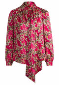 Langärmelige Bluse aus leuchtend pinkem Stoff mit floralen Mustern in Weiß und Gelb, einer Schleifenkragen und gerafften Schultern.