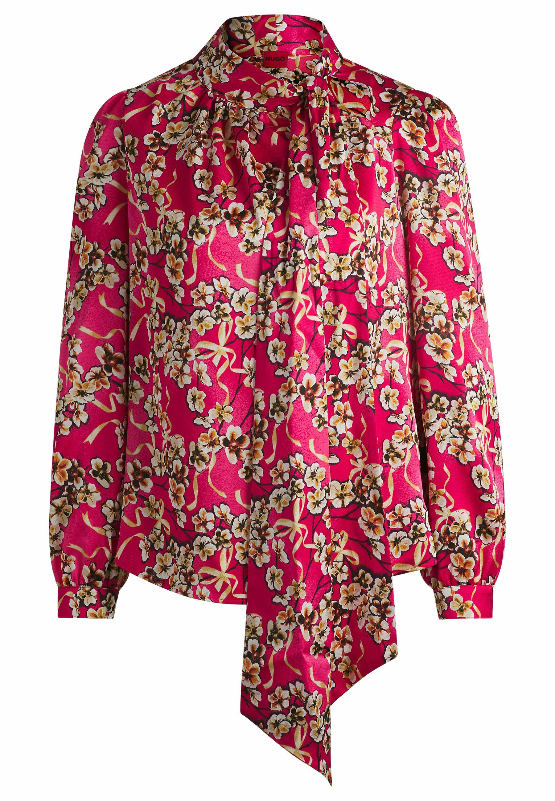 Langärmelige Bluse aus leuchtend pinkem Stoff mit floralen Mustern in Weiß und Gelb, einer Schleifenkragen und gerafften Schultern.