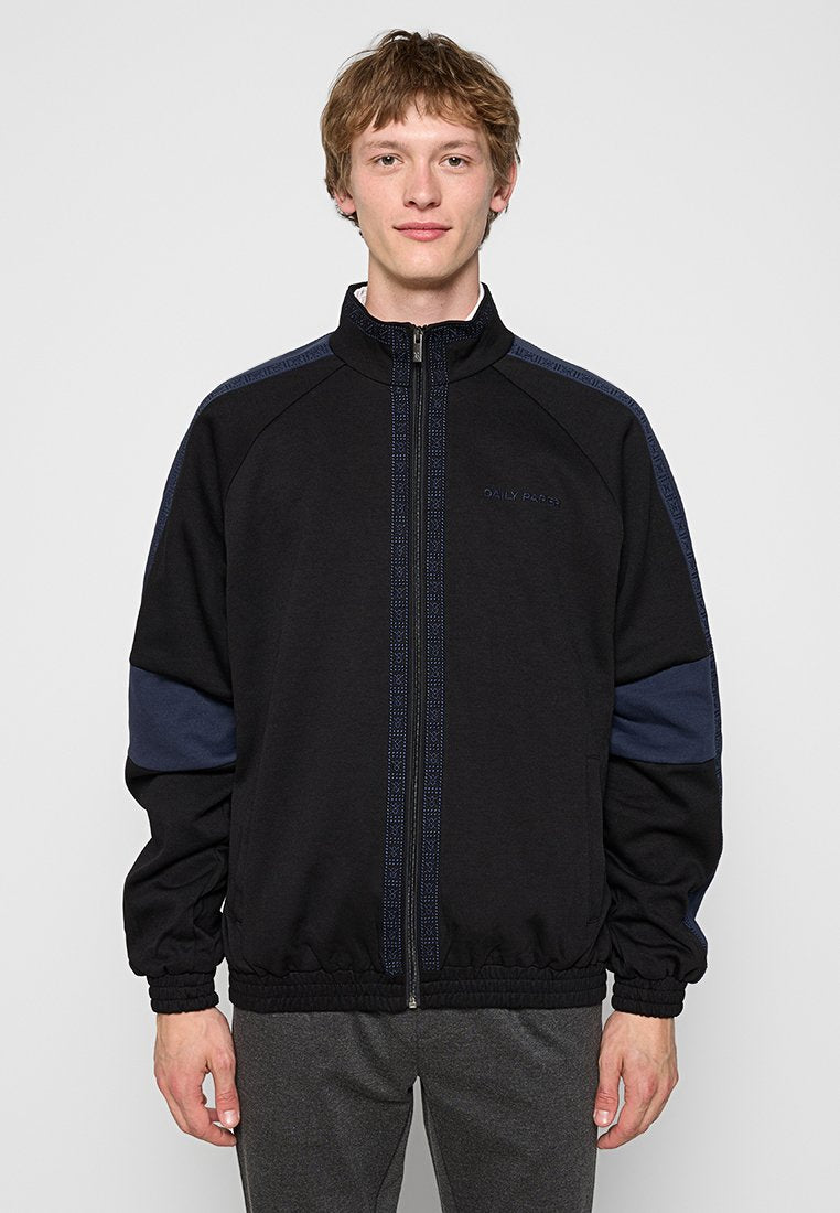 Schwarze Zip-Jacke mit marineblauen Akzenten und elastischen Bündchen. Hergestellt aus weichem Stoff, mit Stehkragen und dezentem Logo-Detail.